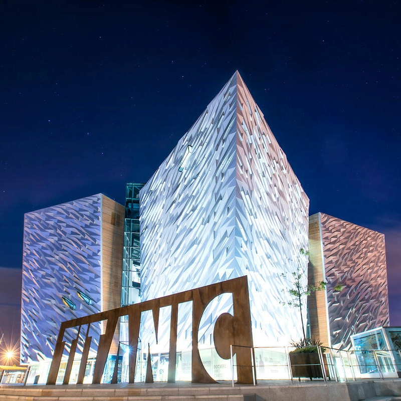 Titanic Belfast illuminato di notte, con la sua facciata argentata angolare e l'iconico cartello del Titanic a Belfast, nella contea di Antrim.