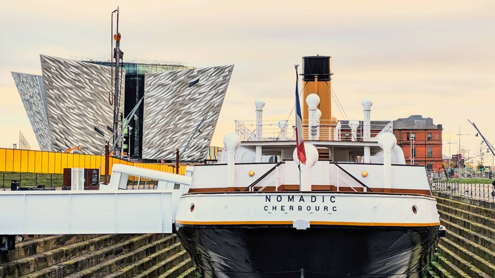 Die SS Nomadic, die im Trockendock vor Anker liegt, dahinter emporragend das moderne Titanic Belfast-Gebäude.