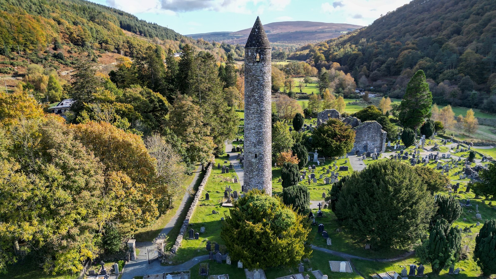 Glendalough round tower and cathedral ruins among autumn trees in Wicklow Mountains National Park.
