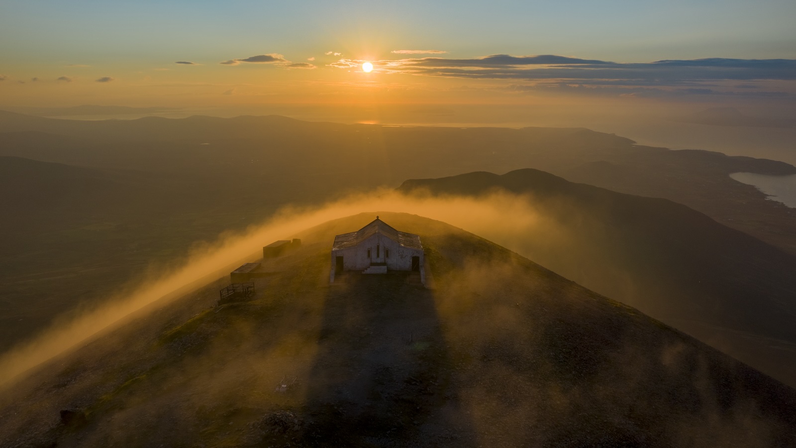 Puesta de sol sobre la cima del Croagh Patrick, con la capilla envuelta en niebla y luz dorada.