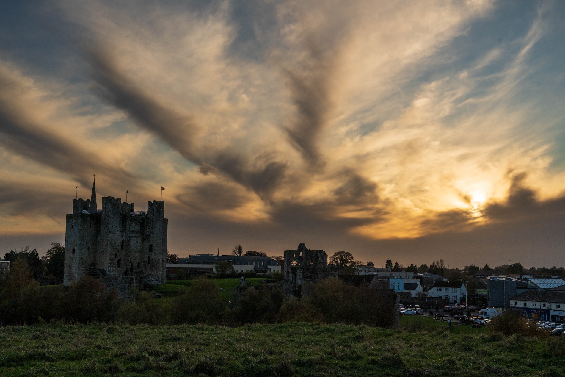 Trim Castle in County Meath rises above the surrounding town beneath a dramatic golden sunset and sweeping clouds.