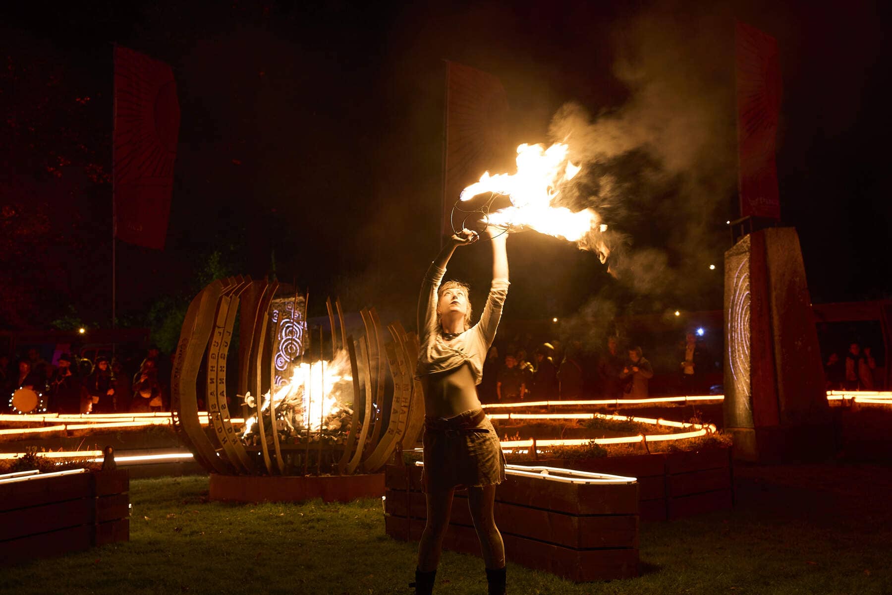 Performer raises flaming props during a night-time fire ceremony, surrounded by glowing installations at the Púca Festival.