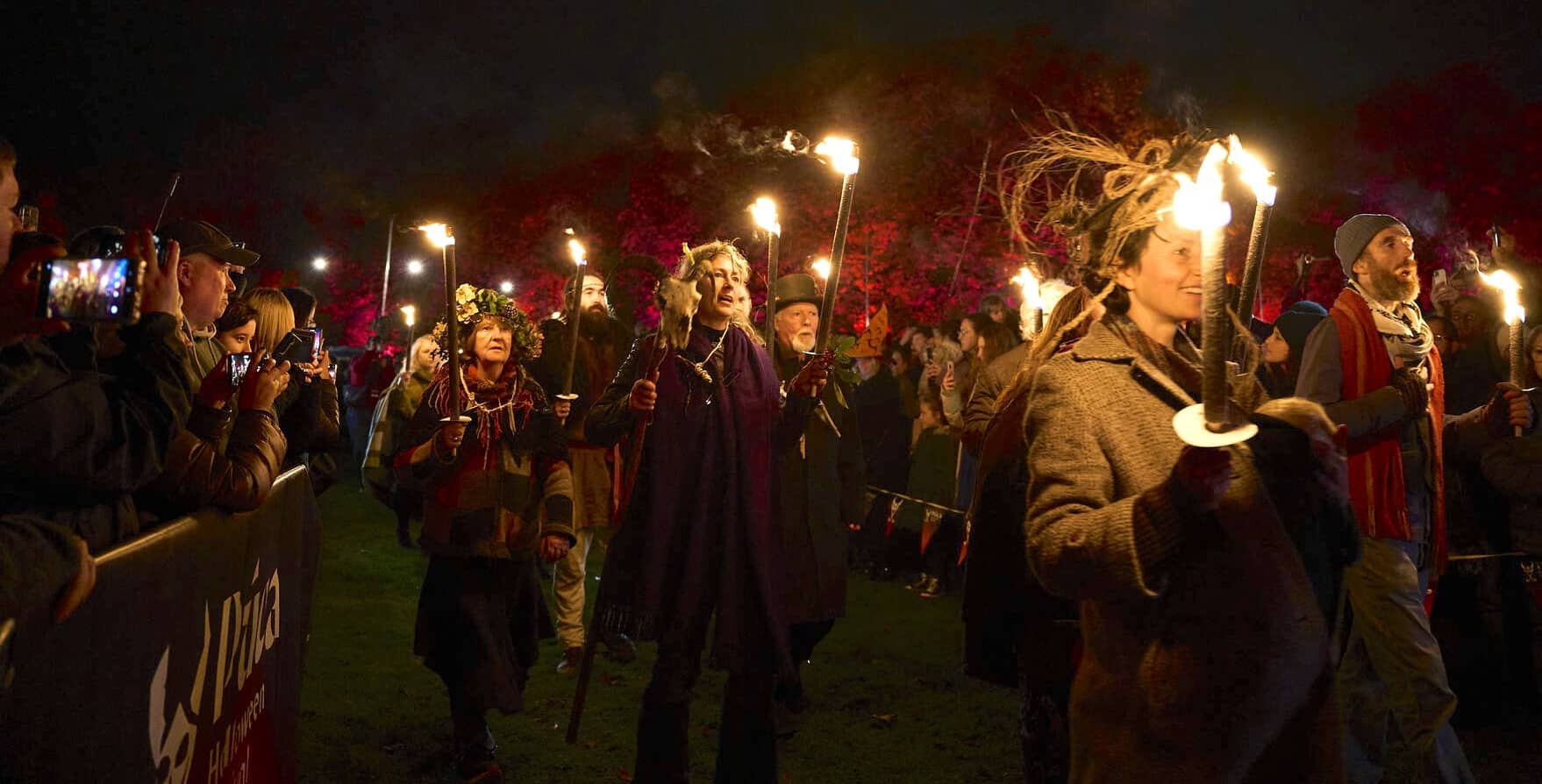 People in costume walk through a night-time torchlit procession, watched by crowds during the Púca Festival in Meath.
