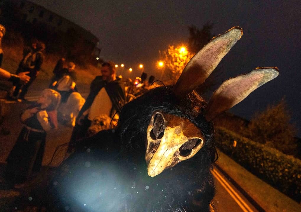 Close-up of performer in eerie horned skull mask and long black fur costume during night-time Púca Festival parade in Meath.