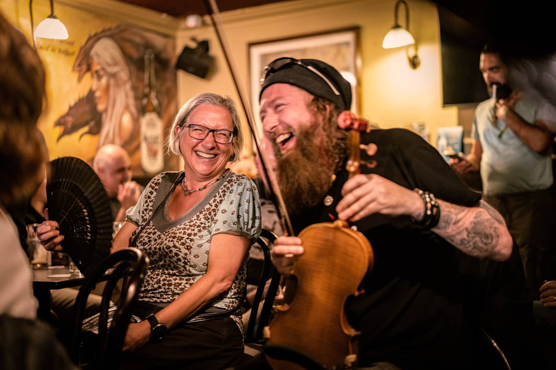 Musician laughing with a woman during a lively traditional music session in McHugh's pub in Belfast.
