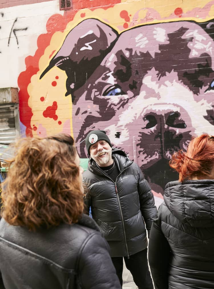 Un guía charla con los visitantes junto a un llamativo mural de un perro en un callejón de Belfast durante una visita guiada de arte urbano.