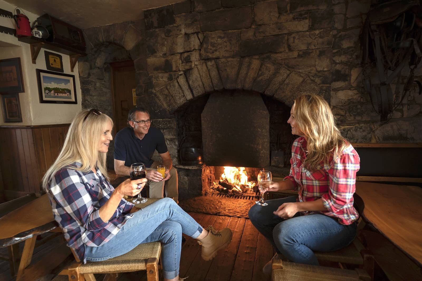 Amigos relajándose junto a una chimenea de piedra en el pub y restaurante Cassidy's, en Burren, condado de Clare, disfrutando de unas copas y de un ambiente cálido y rústico.