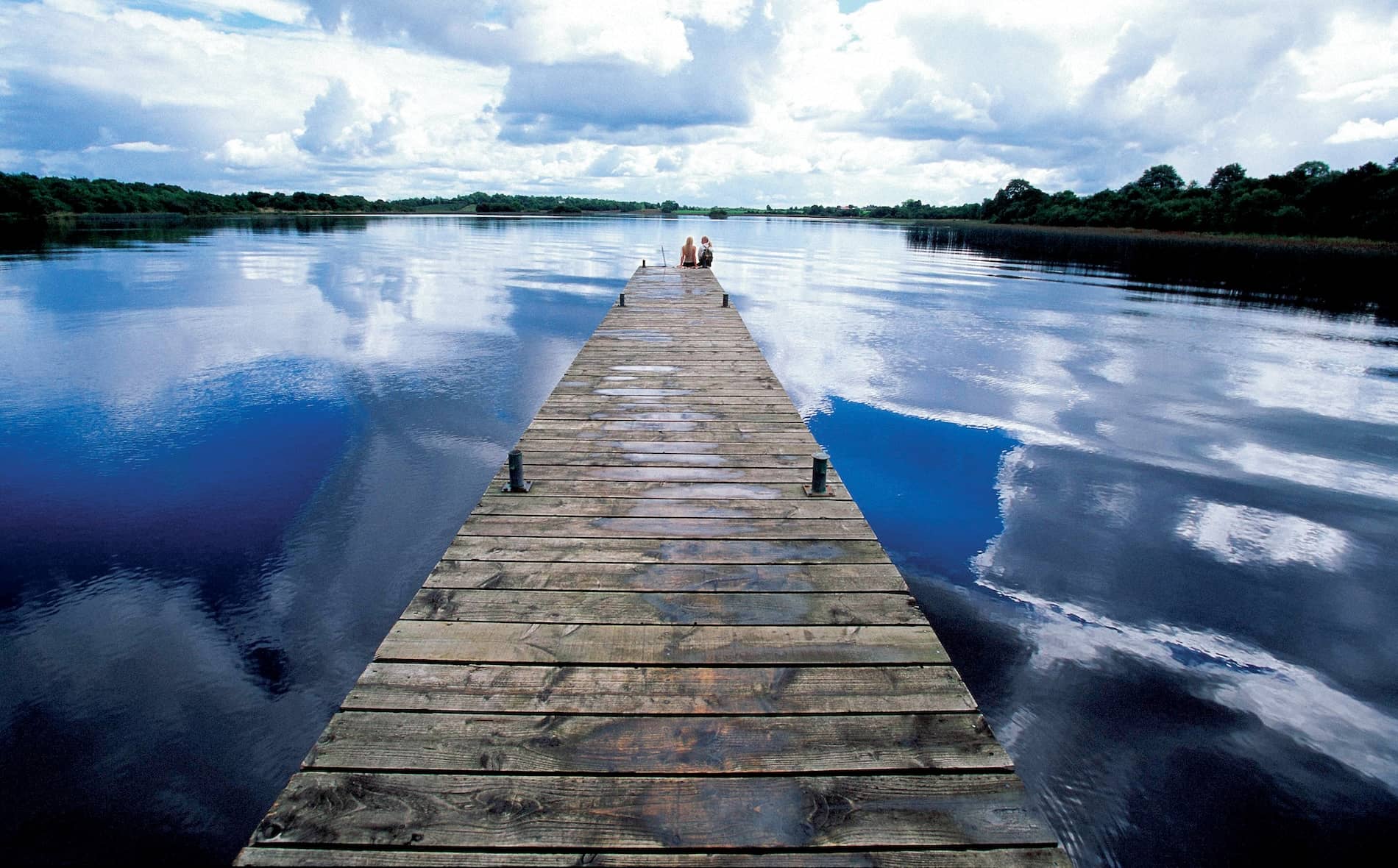 Wooden jetty stretching into the calm waters of Lough Erne in County Fermanagh beneath dramatic reflected skies.