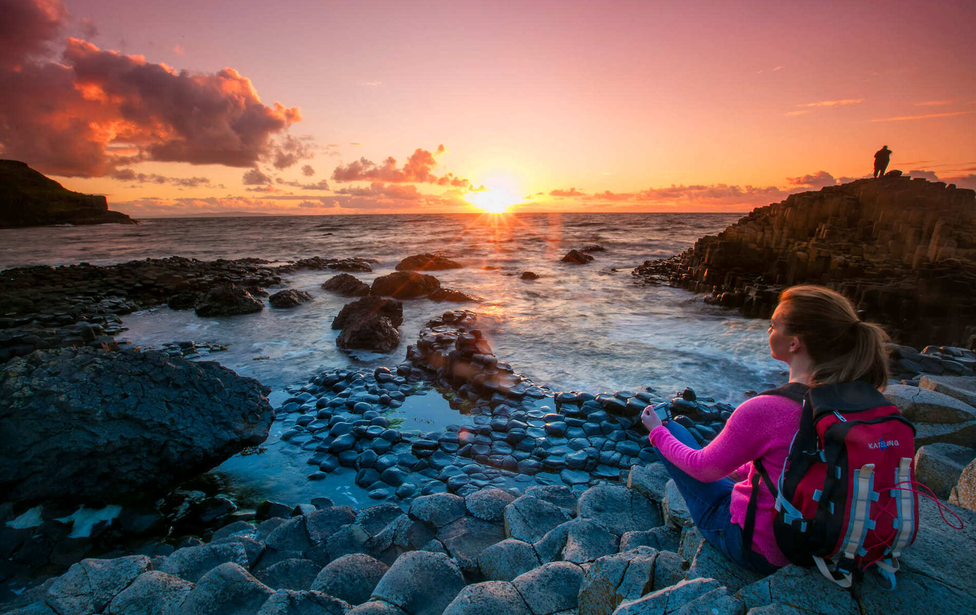Traveller watching sunset over the sea from the basalt rocks of the Giant’s Causeway in Antrim.