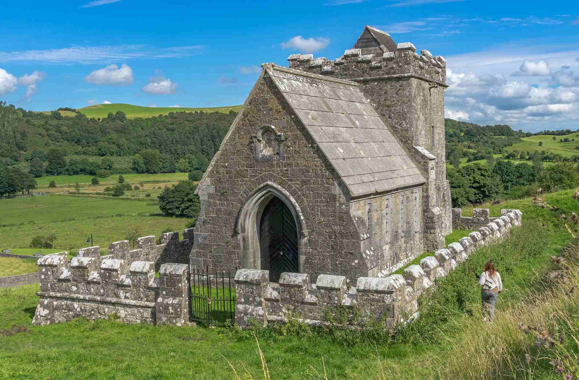 Small stone church at Fore Abbey, enclosed by a low wall, with rolling hills behind.