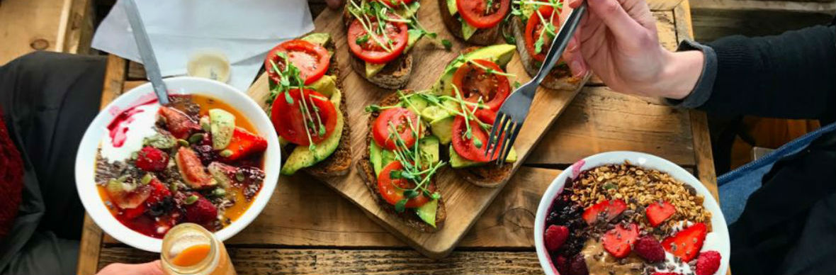 Healthy brunch of avocado toast with fresh tomato, plus bowls of fruit, yoghurt and granola.