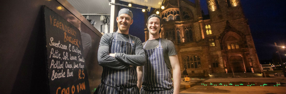 Two smiling chefs in striped aprons outside Pyne 'N' Pommes a street food truck in Derry~Londonderry.