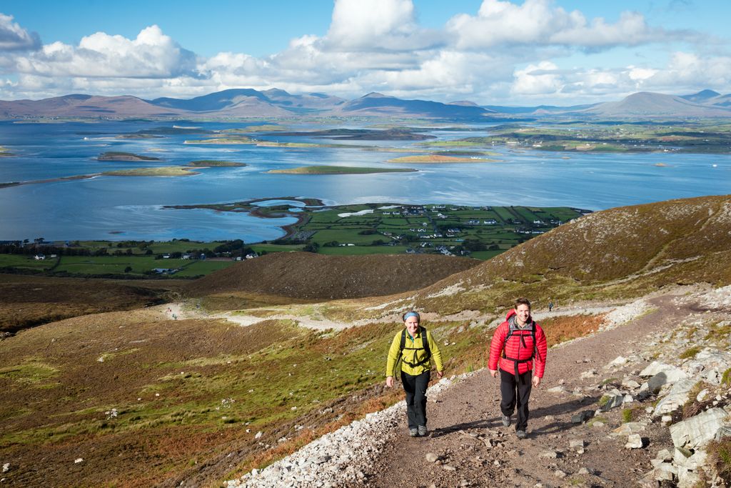 Two hikers climb Croagh Patrick trail in County Mayo with Clew Bay coastline behind them.