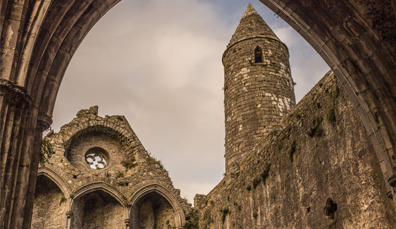 View through the archways of the Rock of Cashel ruins, with its tall round tower framed by weathered Gothic stone.