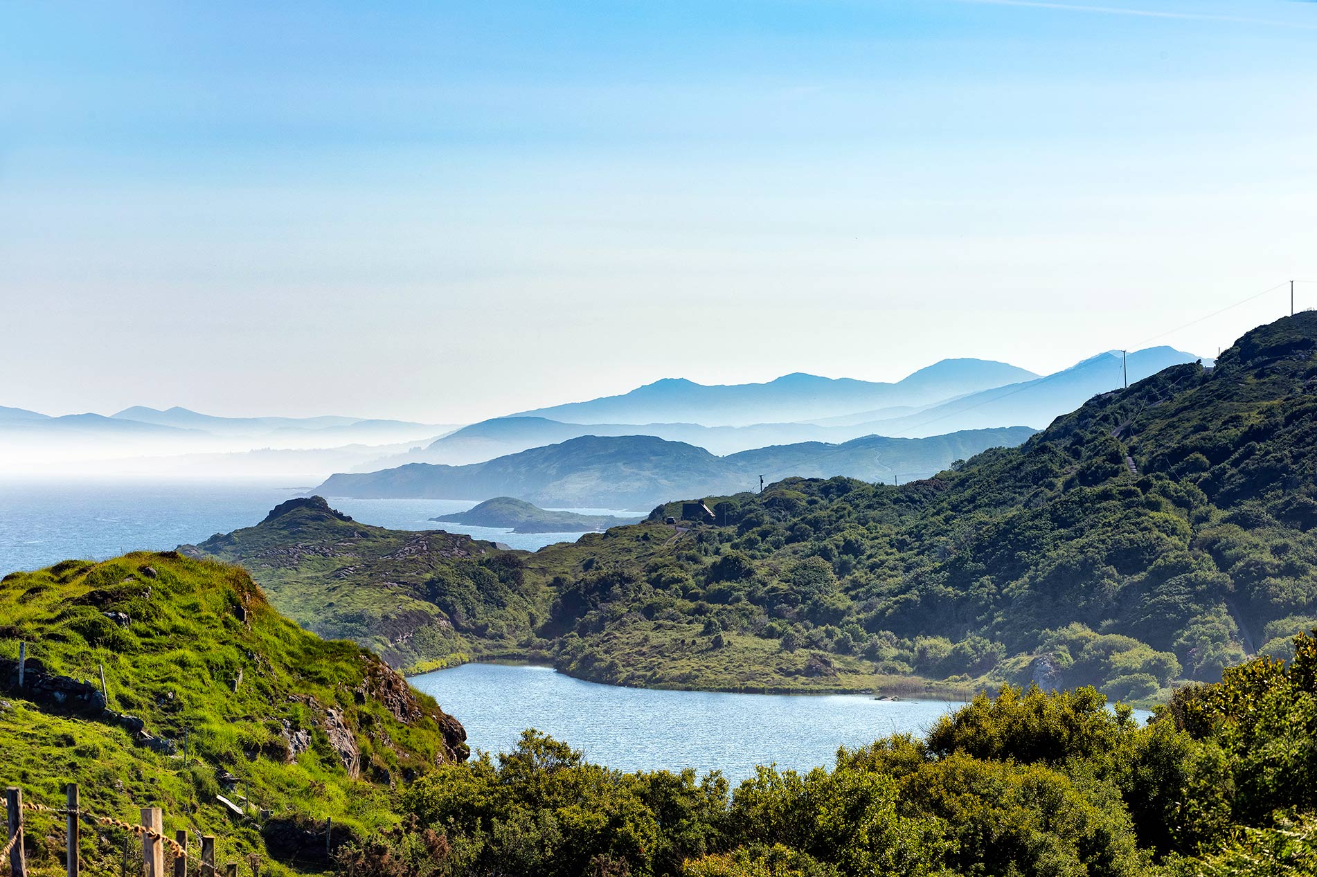 Uitzicht op Derryvegal Lough met groene heuvels en gelaagde blauwe bergen langs de kustlijn van het schiereiland Beara.