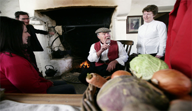 Un uomo che racconta storie davanti al caminetto in un tradizionale cottage irlandese presso l'Ulster American Folk Park nella contea di Tyrone.