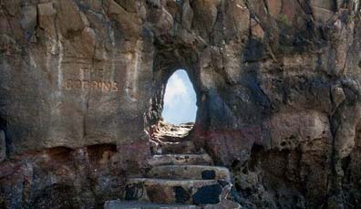 Scalini in pietra che conducono attraverso un'apertura nella roccia a forma di ovale a The Gobbins, incorniciando il cielo oltre.