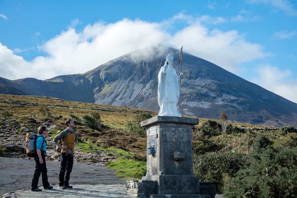 Walkers stand near St Patrick statue on Croagh Patrick pilgrimage path in County Mayo.