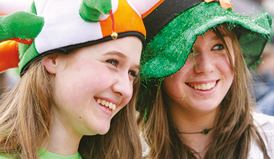 Deux jeunes femmes souriantes coiffées de chapeaux tricolores et en forme de trèfle le jour de la Saint Patrick.