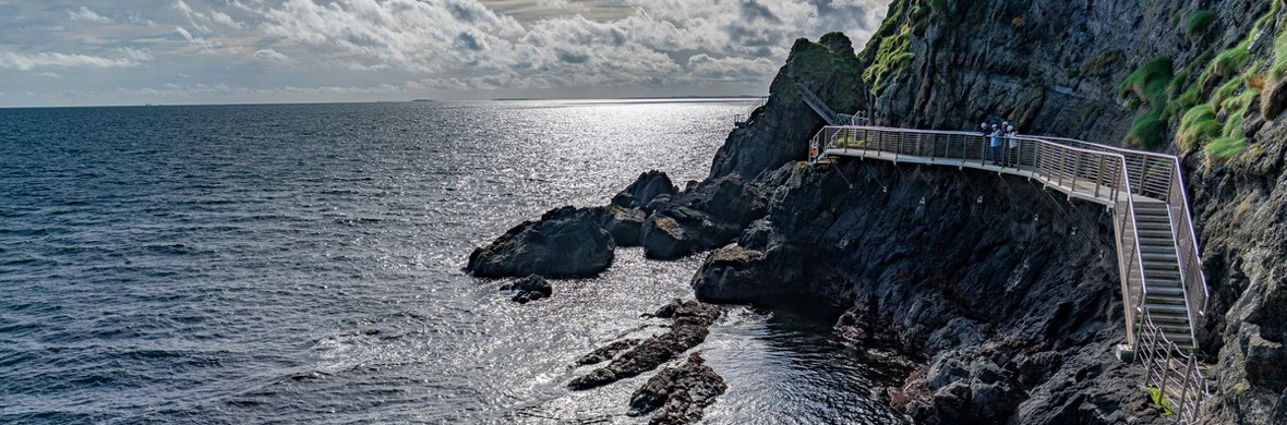 Vista panoramica sulla passerella di The Gobbins che si allunga lungo le spettacolari scogliere marine sopra le acque luccicanti dell'oceano.