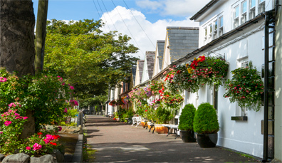 Charmante Dorfstraße in Killough, Grafschaft Down, Irland, gesäumt von weißgetünchten Cottages und hängenden Blumenkörben.