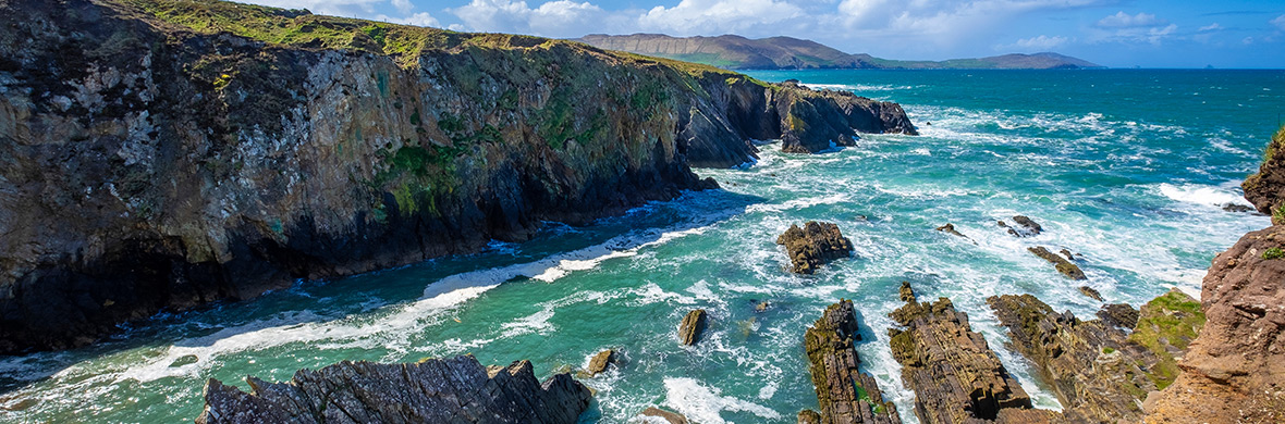 Steile Klippen entlang der Küste von Allihies in West Cork mit Wellen, die gegen die zerklüfteten Felsen brechen.