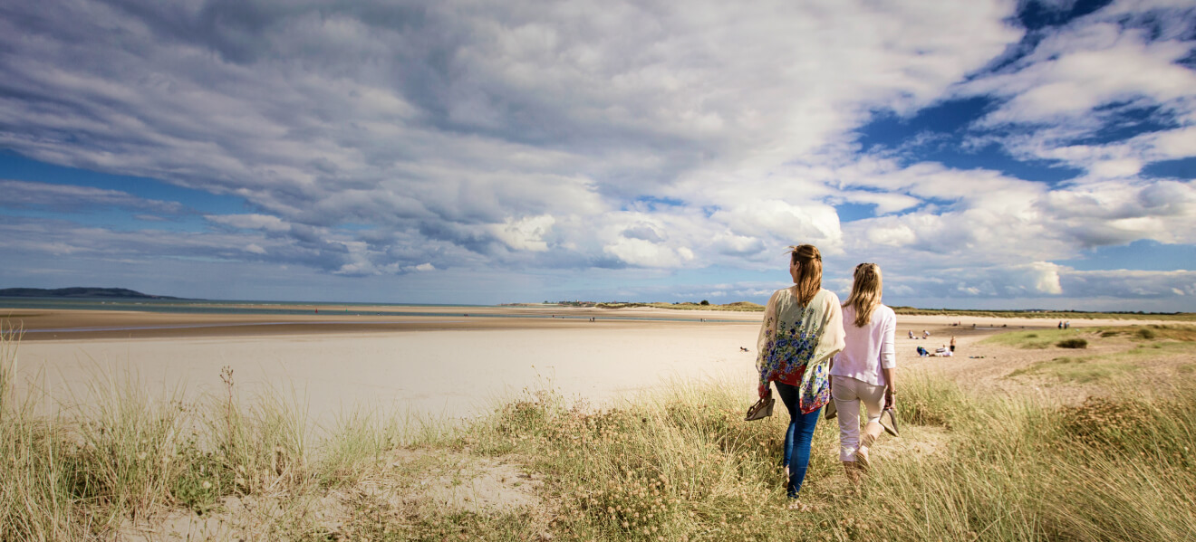 Two girls walking through the sand dunes on Malahide Beach in Dublin on a bright summer day.