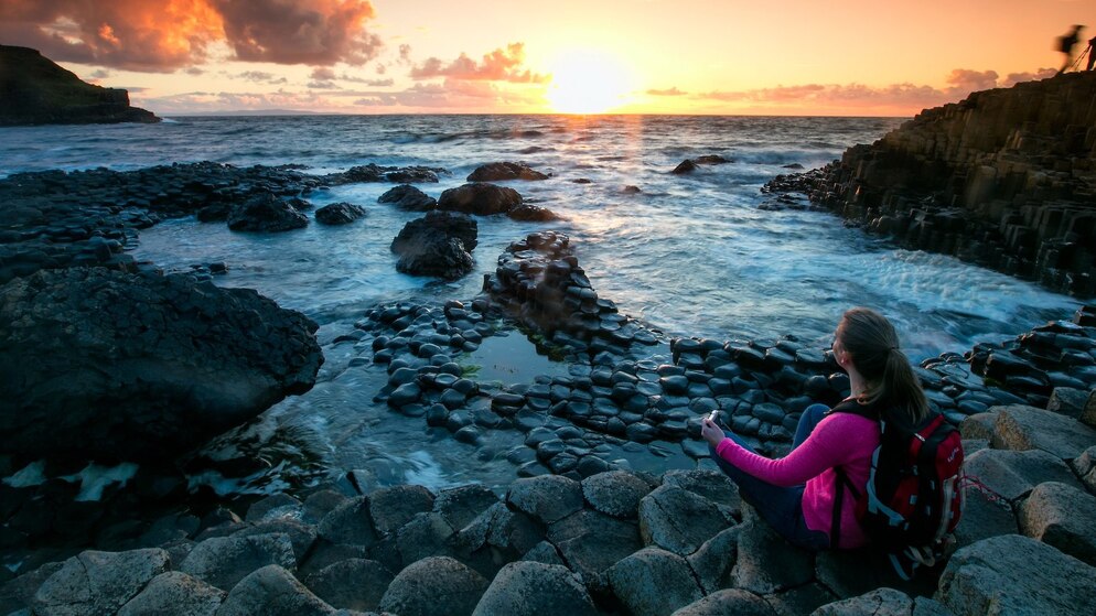 Visitor at Giant’s Causeway, Northern Ireland, watching sunset over the sea.
