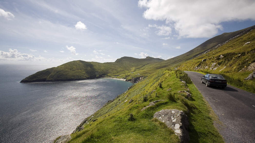 Mountain backdrop with winding road alongside a lake on a cloudy day in Connemara, Ireland.