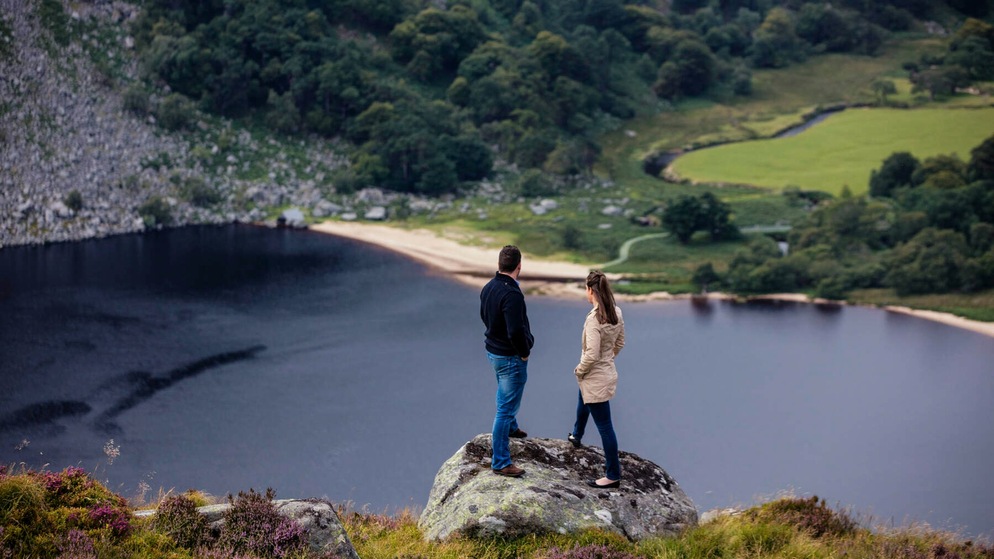 Couple stands on a rock overlooking scenic Lough Tay in County Wicklow, a filming location for TV shows made in Ireland.