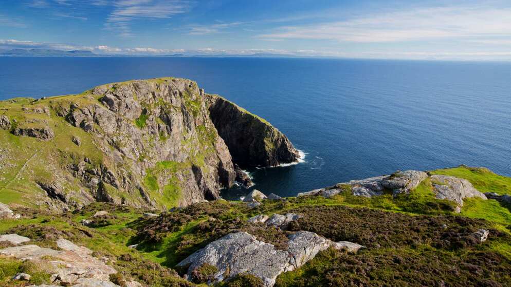 Une falaise rocheuse s'avance dans l'Atlantique sous un ciel bleu clair dans cette vitrine estivale du littoral irlandais.