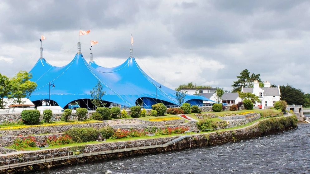 Grande tenda blu del festival con le bandiere vicino a giardini e case sul fiume al Galway International Arts Festival.