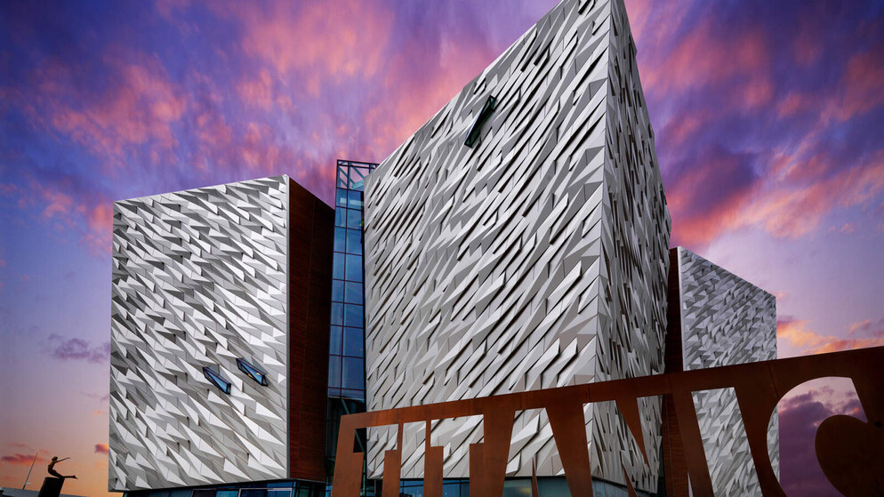 Striking Titanic Belfast museum with angular design lit by pink sunset sky in Northern Ireland.
