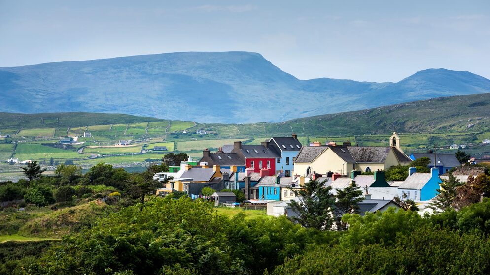 Kleurrijke huizen in het dorp Allihies liggen onder glooiende groene velden en ruige bergen op Ierlands Wild Atlantic Way.