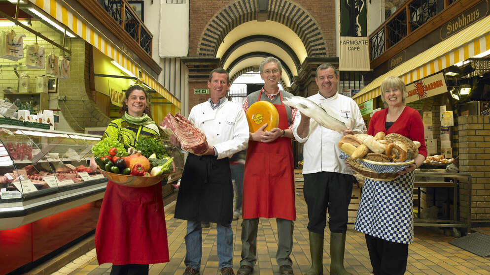Producers holding Irish food including cheese, bread, fish and vegetables.