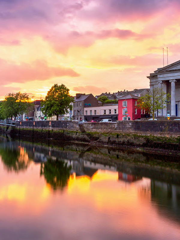 Het stadhuis en de georgiaanse gebouwen in Cork weerspiegeld in de rivier de Lee bij het vallen van de avond, onder een diepblauwe avondhemel.