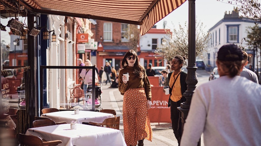 Woman in sunglasses walks with coffee on Dalkey’s main street during the Dalkey Book Festival in County Dublin.