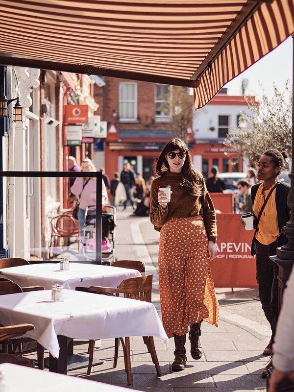 Woman in sunglasses walks with coffee on Dalkey’s main street during the Dalkey Book Festival in County Dublin.