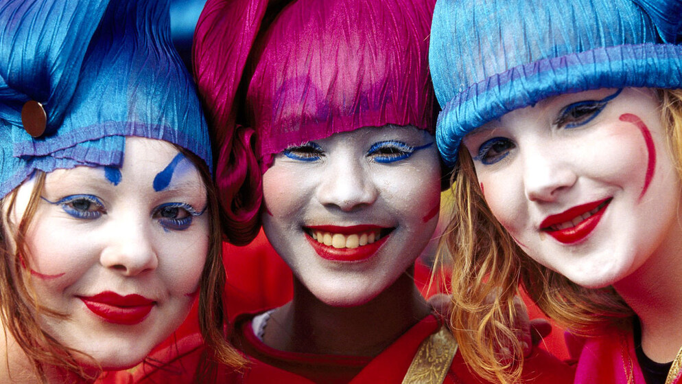 Three performers in colourful wigs and painted faces smile during a St Patrick’s Day parade in Ireland.