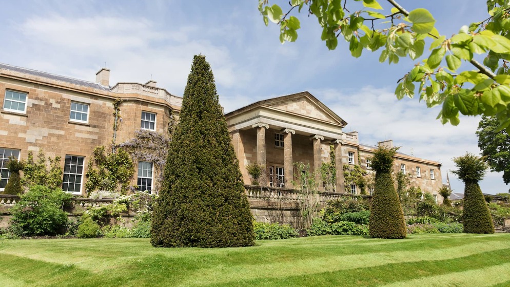 Elegant Georgian-style Hillsborough Castle in County Down with trimmed hedges and landscaped gardens under a spring sky.
