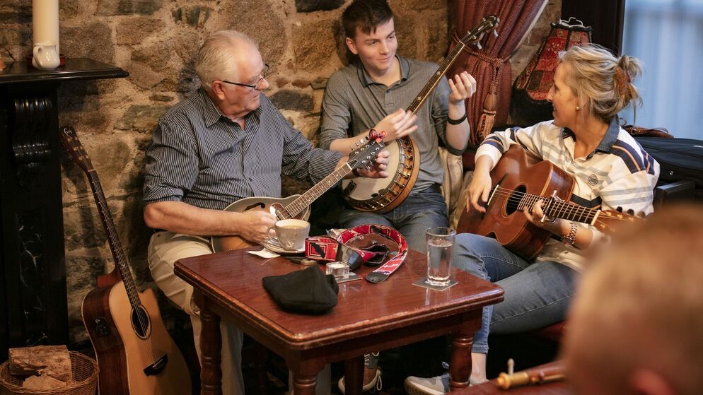 Drei Musiker sitzen in einem gemütlichen Pub und spielen während einer traditionellen irischen Musiksession Mandoline, Banjo und Gitarre.