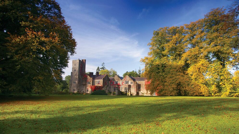 Manor house retreat framed by autumn trees at Belle Isle Estate, County Fermanagh, under a deep blue sky.