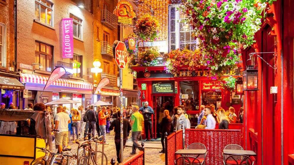 Crowds enjoying nightlife on a colourful street in Dublin’s Temple Bar, with pubs, lights and hanging flowers.