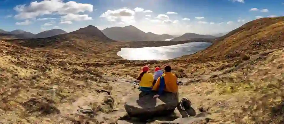 Group resting on a rock while overlooking a lake and mountain views in the Mourne Mountains, County Down.