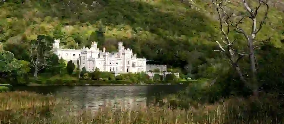 Kylemore Abbey reflected in a Connemara lake, surrounded by forested hills in County Galway.