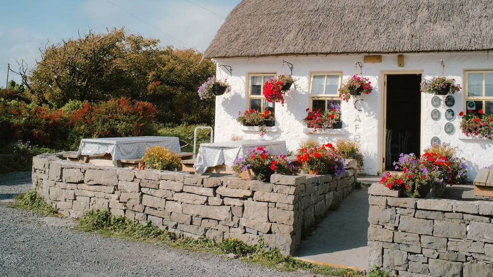 Coastal café cottage with a thatched roof and colourful flower baskets, on the Aran Islands, County Galway.