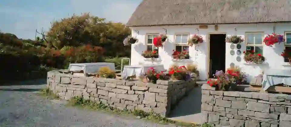Coastal café cottage with a thatched roof and colourful flower baskets, on the Aran Islands, County Galway.