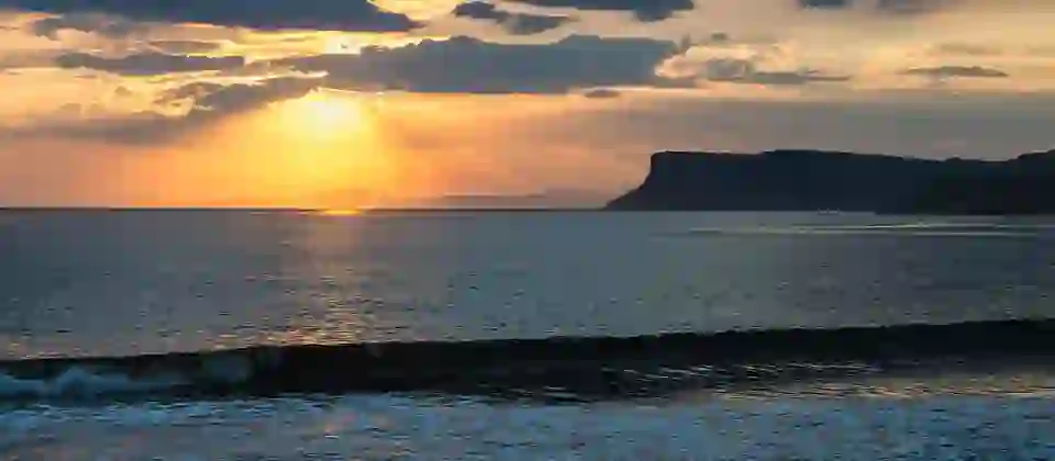 Sunset over Fair Head in County Antrim with golden light across the sea and waves rolling onto the shore.