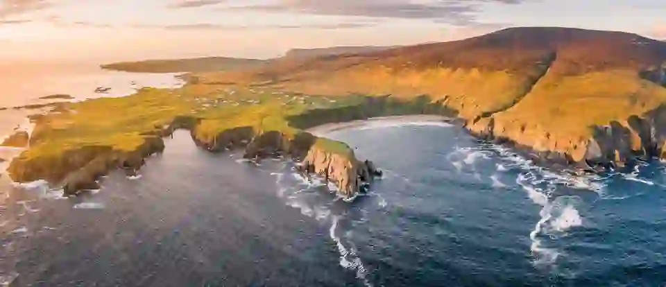 Aerial view of Silver Strand beach in County Donegal with rugged cliffs, rolling hills and Atlantic coastline at sunset.