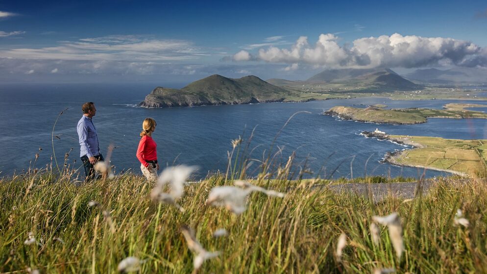 Two walkers overlook a dramatic coastline in Ireland, highlighting emergency contact information for visitors.